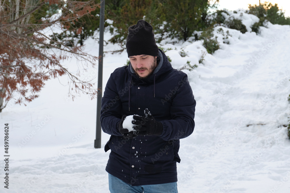 Young caucasian man making a snowball in a park