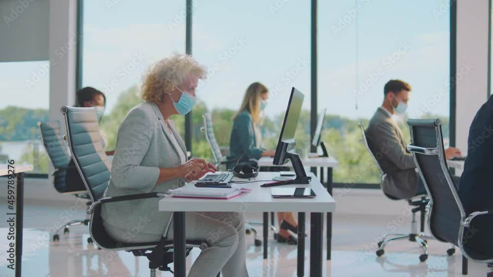 Working in COVID-19 world pandemic. Colleagues in office wearing protective face mask. Modern open space office interior. Working in COVID-19 world pandemic. Colleagues in office wearing protective face mask. Modern open space office interior.