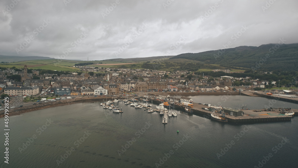 Ships, yachts at sea bay aerial. Cityscape with ancient architecture landmark at ocean pier town Campbeltown, Scotland, Europe. Dramatic streets: old buildings at highway with driving cars at dusk day