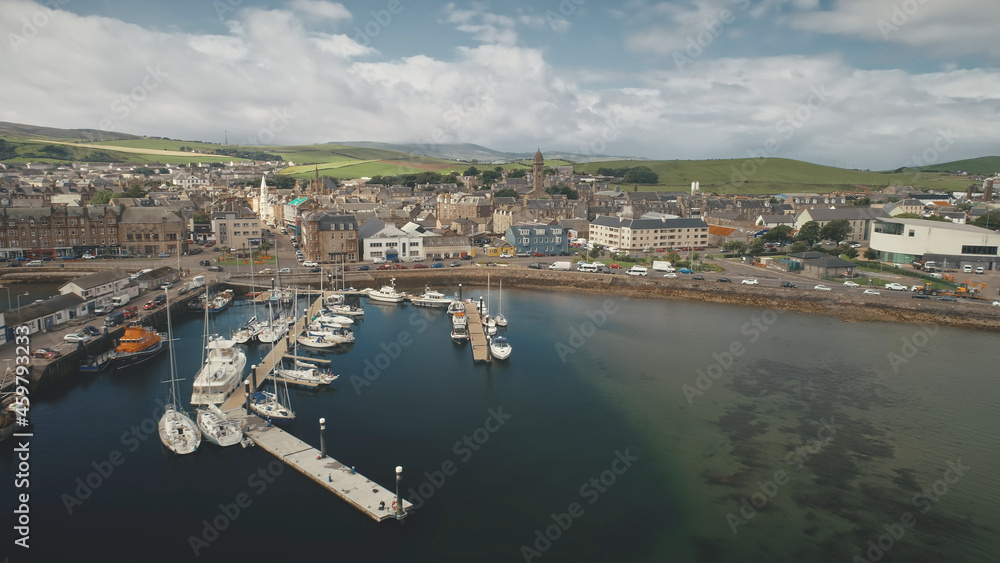 Traffic road at sea bay coast aerial. Pier town with old buildings. Ships and yachts at wharf. Marina seascape at urban highway with cars, vans, trucks. Campbeltown cityscape, Scotland, Europe