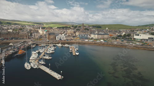 Traffic road at sea bay coast aerial. Pier town with old buildings. Ships and yachts at wharf. Marina seascape at urban highway with cars, vans, trucks. Campbeltown cityscape, Scotland, Europe