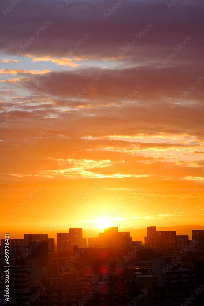 都市の夜明け、早朝ビルの隙間から太陽が昇り辺りはオレンジ色に染まる。ビルはシルエットに浮かぶ