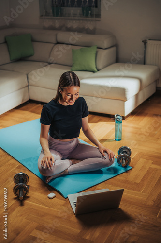 Woman using dumbbells and laptop while working out at home