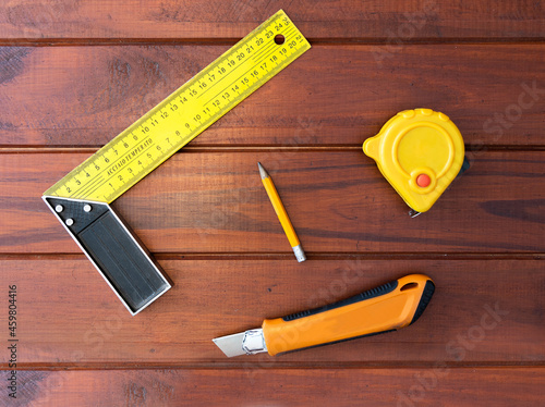 lapiz de grafito en medio de una escuadra de metal, una cinta metrica y un cutter en una mesa de trabajo