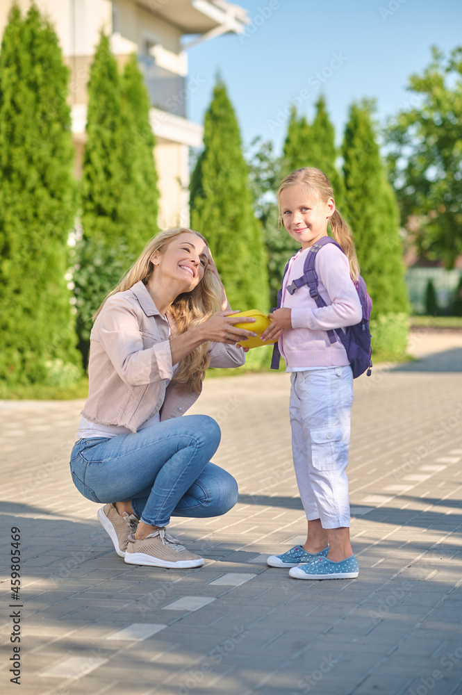 Joyful woman giving lunchbox to little girl Joyful woman giving lunchbox to little girl