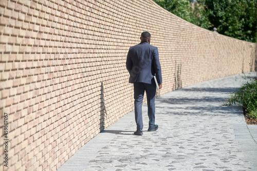 A dark-skinned man walking along the brick wall