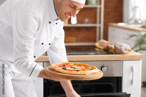 Italian chef taking tasty pizza from oven in kitchen © Pixel-Shot
