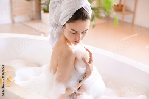 Young woman with loofah taking relaxing bath at home photo