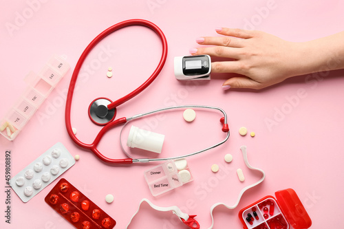 Woman with pulse oximeter, stethoscope and pills on color background