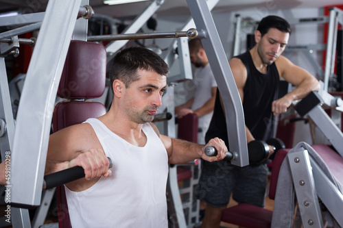Sporty guy training muscles of arms and shoulder girdle on fitness machine in gym