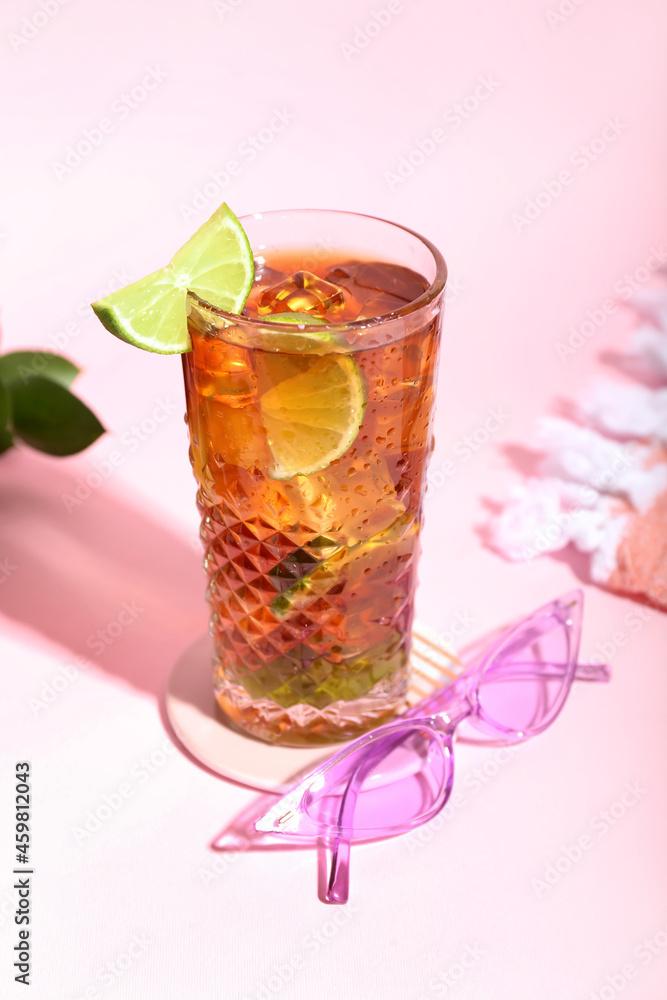 Glass of refreshing Long Island iced tea with lime and stylish sunglasses on color background Glass of refreshing Long Island iced tea with lime and stylish sunglasses on color background