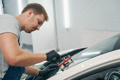 Mechanic man is applying glue on cracked front window of car closeup