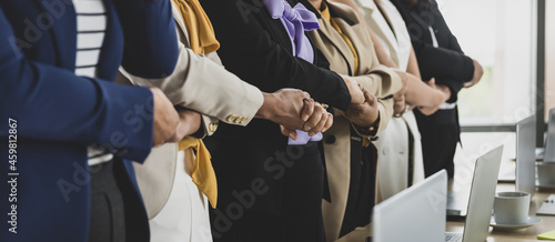 Selective focus on five Asian business women in formal suits torso standing and holding hands together in office