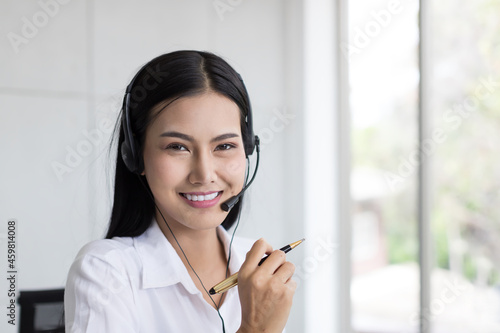 Asian call center female worker at work. Smiling female customer support operator with headset working in the office. Contact center and customer service by headphone concept photo