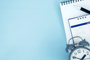 pen with white spiral notepad  and alarm clock calendar placed on blue background , business meeting agenda schedule, travel planning booking or a project event milestone and reminder concept.