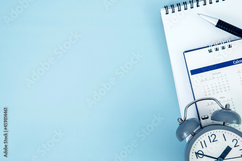 pen with white spiral notepad  and alarm clock calendar placed on blue background , business meeting agenda schedule, travel planning booking or a project event milestone and reminder concept. photo