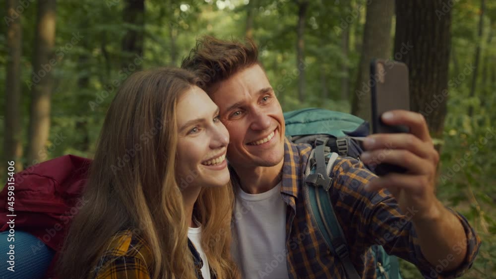 Happy couple in love making selfie on smartphone, making photos during hiking walk in forest, tracking shot, slow motion Happy couple in love making selfie on smartphone, making photos during hiking walk in forest, tracking shot, slow motion