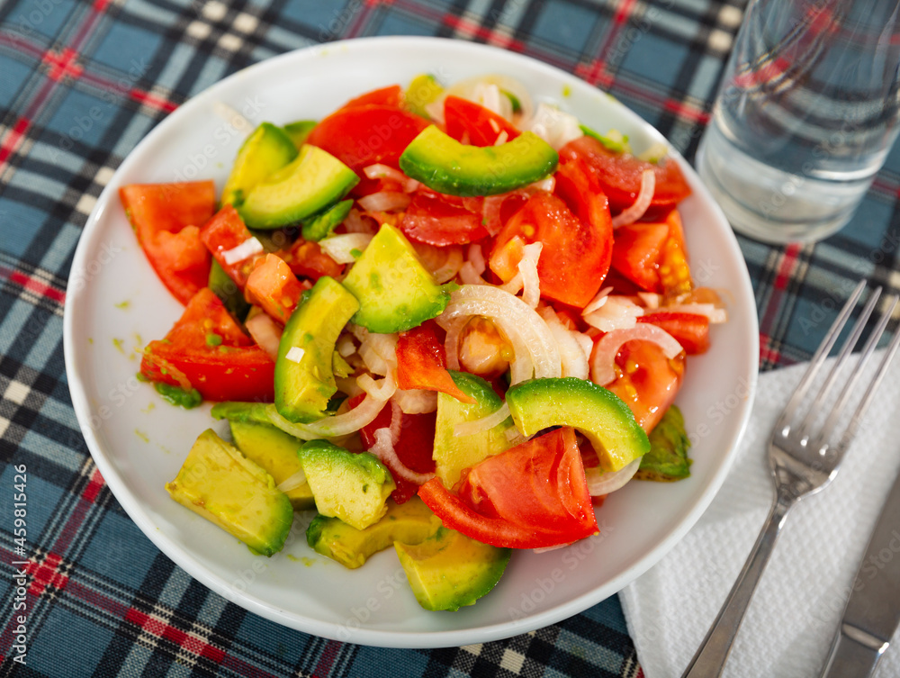 Healthy vegetable salad of sliced fresh tomatoes, avocado and onion with olive oil