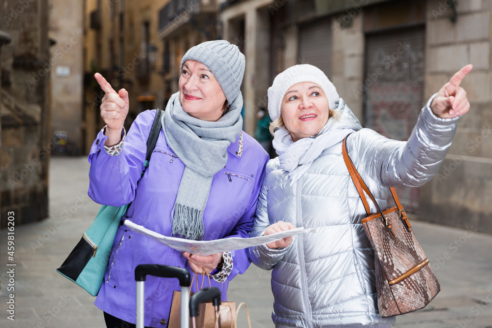 Senior woman with female friend traveling together looking for destination with city map.