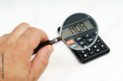 A man looks through a magnifying glass at a calculator on the screen of which it is written - NDA
