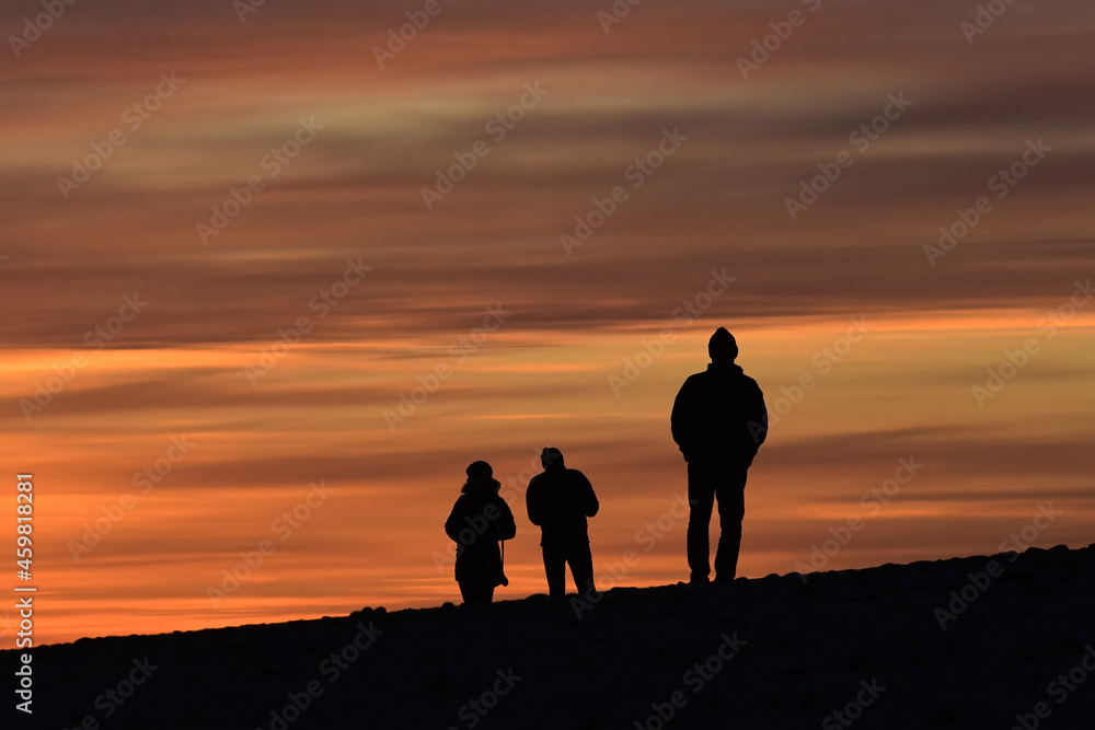 Silhouette of three people walking on the beach at sunset in Homer, Alaska.