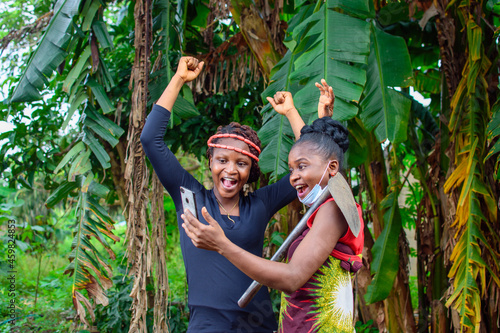 Fotografija A female african farmer with nose mask and a farming hoe on her shoulder happily