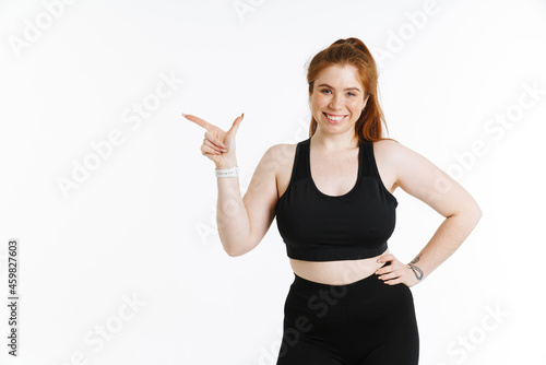 Young ginger woman smiling while pointing finger aside