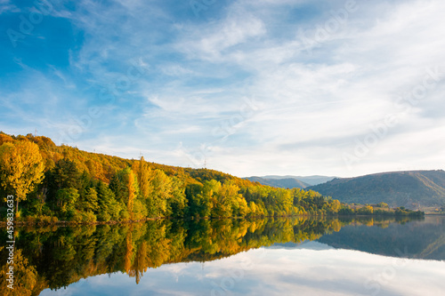 beautiful autumn landscape by the lake at sunset. trees in colorful foliage and forested apuseni mountains reflecting in the water surface. clouds on the sky in evening light