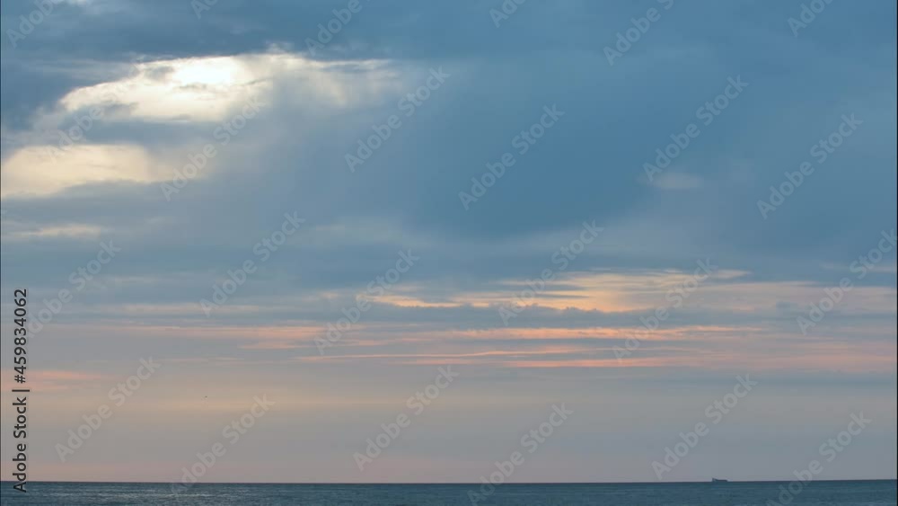 Dark blue clouds glide sideways low above the sea as the sun sets. Sunlight penetrate through the cracks in the clouds. Sea ship sail fast along horizon line. Time lapse video. Dark blue clouds glide sideways low above the sea as the sun sets. Sunlight penetrate through the cracks in the clouds. Sea ship sail fast along horizon line. Time lapse video.
