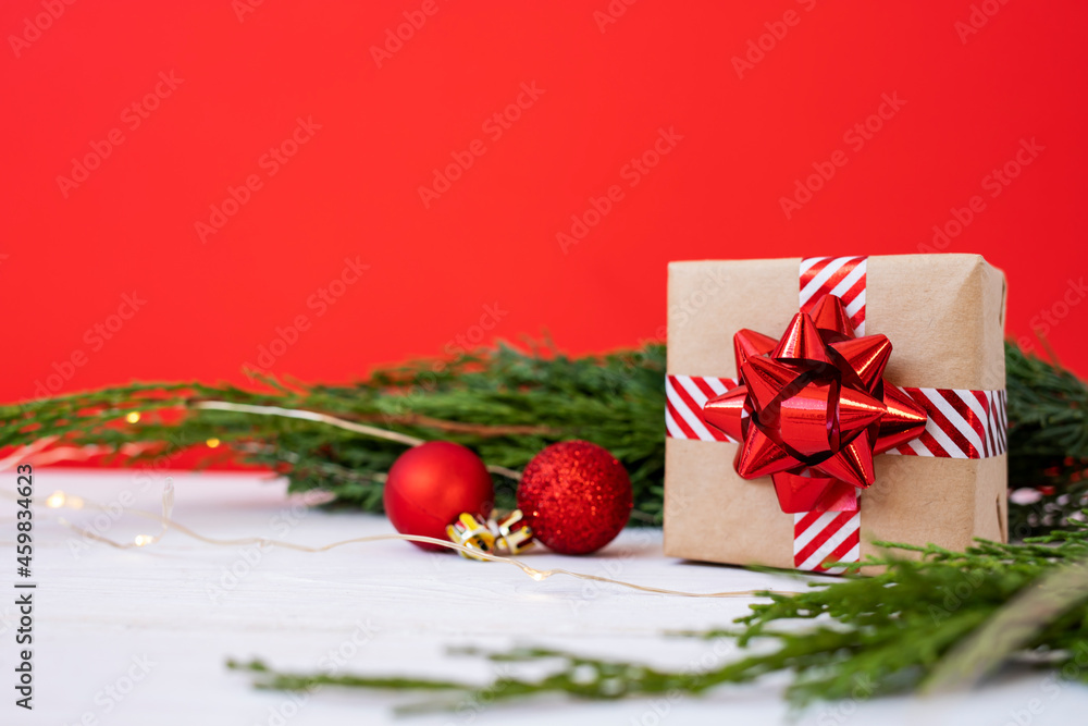 Christmas gift in craft paper on a background of coniferous branches and shiny balls.