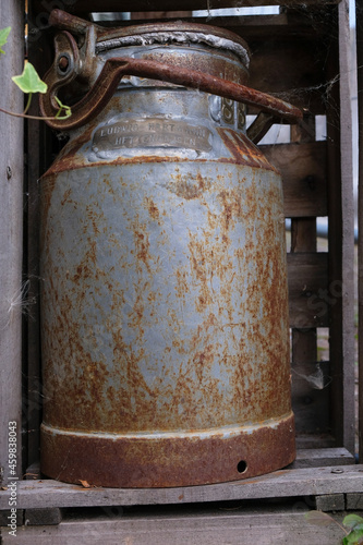 Antique milk can in a wooden box as a garden decoration. On a metal plate the number, the name of the owner, and the name of the community. Vertical image. 