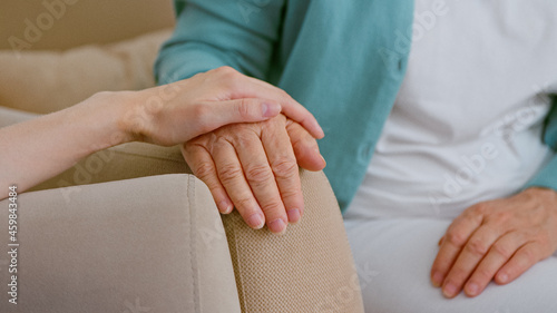 Caregiver cheers up senior lady patient touching hand while sits in armchairs in light room photo
