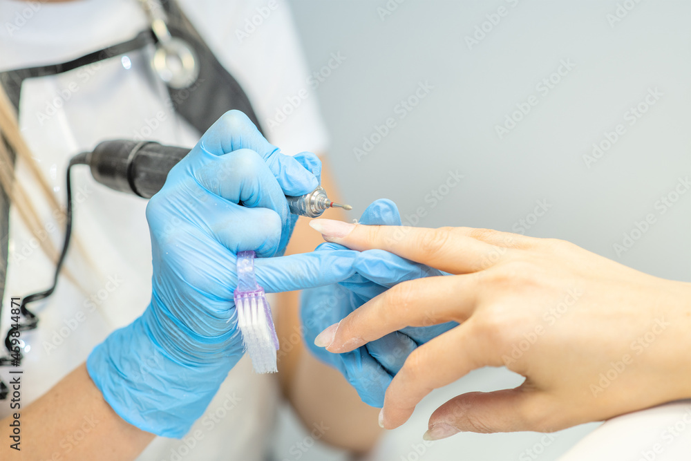 Professional manicure master using electric machine in beauty salon to remove nail polish hands during manicure procedure Professional manicure master using electric machine in beauty salon to remove nail polish hands during manicure procedure