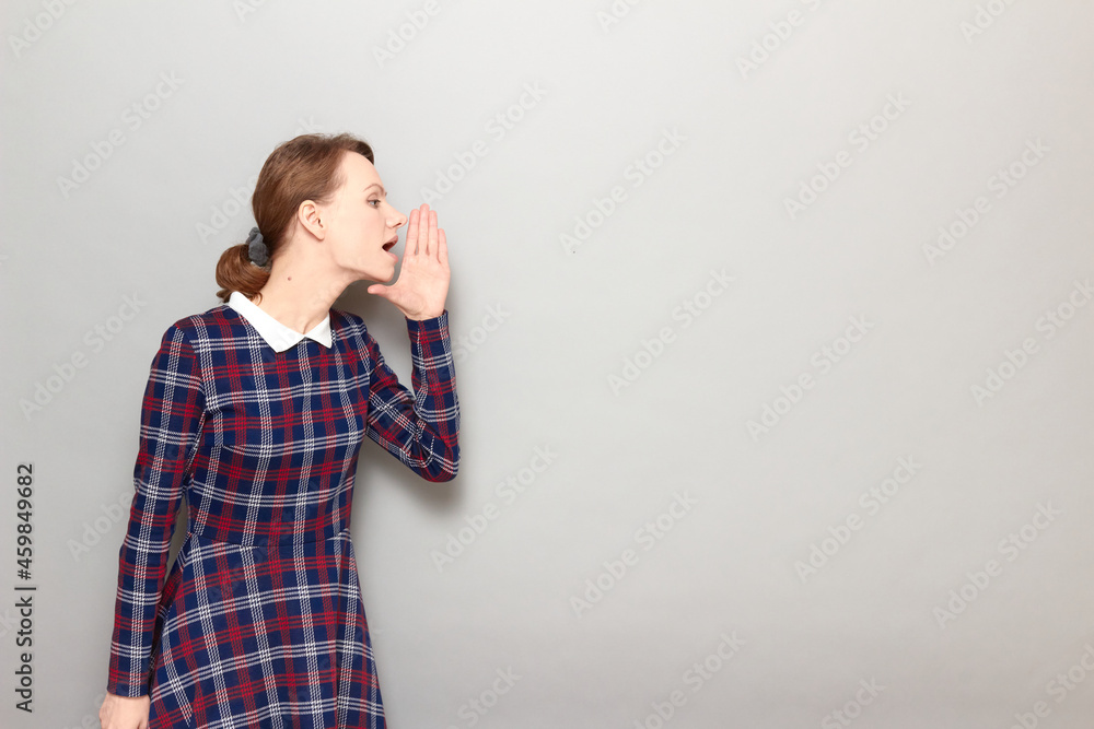 Portrait of young woman screaming loudly to side with hand near mouth Portrait of young woman screaming loudly to side with hand near mouth