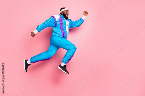 Photo of impressed cute dark skin man wear blue suit headband jumping high running looking empty space smiling isolated pink color background