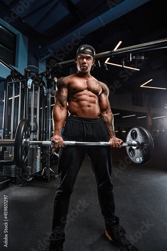 Strong and muscular afro-american man trains on modern equipment in gym. Portrait of muscular pumped up fitness trainer
