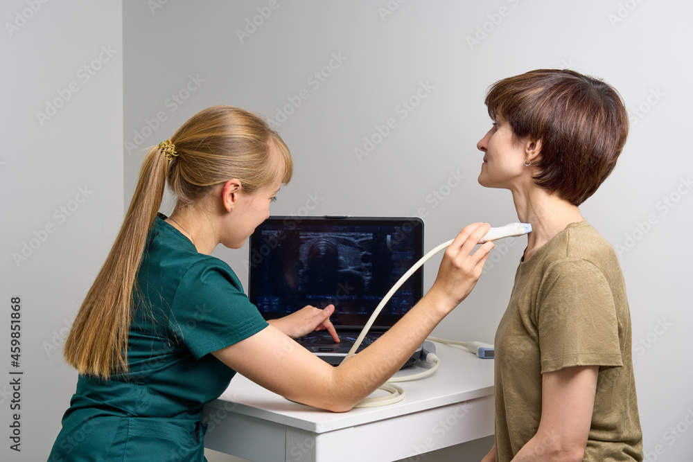 Young doctor doing ultrasound scanning of female patient. Nurse examining throat and blood vessels in neck. Medical professional providing expert assistance in scanning using linear probe Young doctor doing ultrasound scanning of female patient. Nurse examining throat and blood vessels in neck. Medical professional providing expert assistance in scanning using linear probe