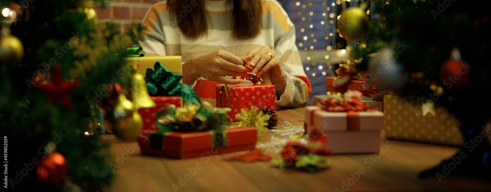 Young woman tighten gorgeous bow on present box on desk as craft working to prepare luxury gift and beautiful ornament for Christmas party decoration to celebrate winter holiday in December