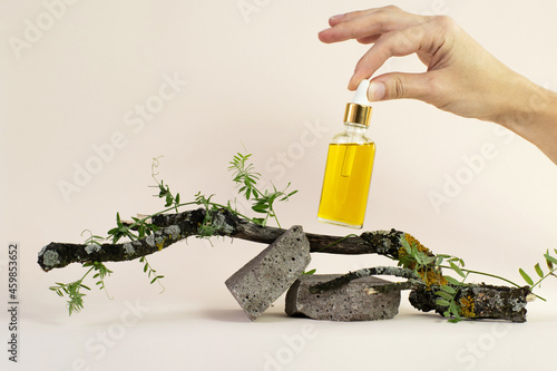 oil cosmetic bottle on a stone podium and wooden branch on beige background. Bottle of essential oil on the natural background. eco friendly care organic product. Spa concept. copy space