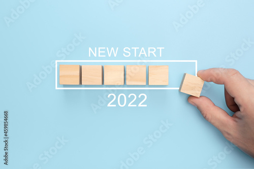 New start 2022 concept. Loading new year 2022 with hand putting wood cube in progress bar. blue background