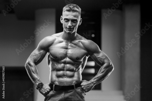 Young athletic man pumping up muscles in the gym at workout. Sport and health care concept background 