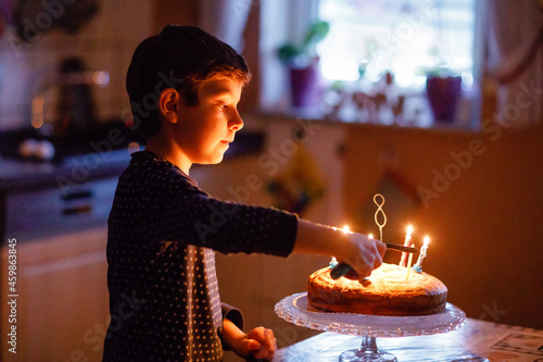 Adorable happy blond little kid boy celebrating his birthday. Child blowing candles on homemade baked cake  indoor. Birthday party for school children  family celebration  fireworks