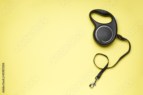 Black retractable dog leash on a yellow background, space for text, flat lay.