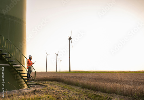 Male technican looking at wind turbine while standing on staircase photo