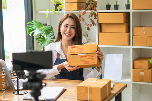 Young asian woman startup small business freelance sitting with parcel box and computer laptop on wood table in living room at home, Online marketing packing box delivery concept
