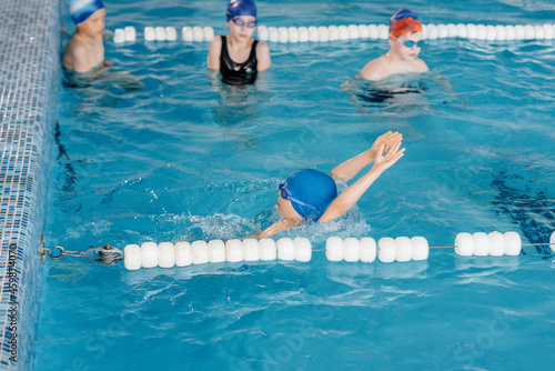 A group of boys and girls train and learn to swim in the pool with an instructor. Development of children s sports.