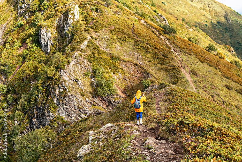 rear view of young woman in yellow hoodie in hood with backpack hiking in picturesque mountain valley healthy active lifestyle digital detox, outdoor activities