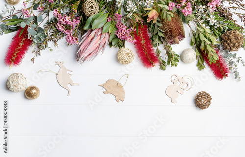 Christmas Background decorated with Australian native wooden animals and flowers - Eucalyptus leaves, Protea, Banksia, Callistemon, Tea Tree and Wax-flowers, on a rustic white background