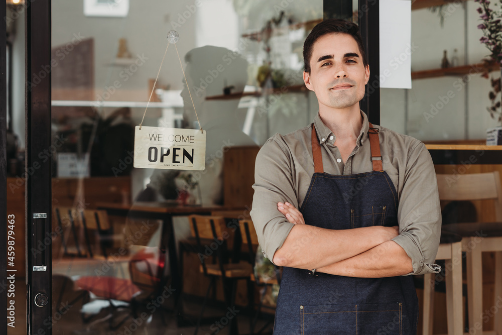 Obraz premium Portrait of a handsome and confident cafe owner standing at the door. Young man standing with his arms crossed looking at camera smiling.