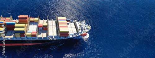 Aerial drone ultra wide top down photo of container cargo tanker ship carrying truck-size colourful containers in deep blue open ocean sea 